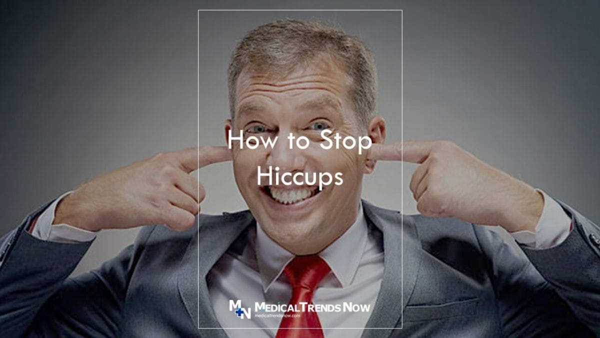 male on an expensive suit and tie sticking his fingers in his ears to remove hiccups